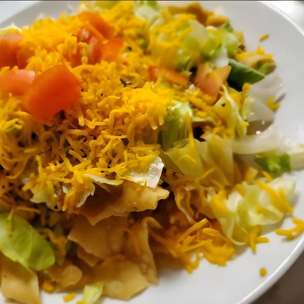 A close-up of a Mexican salad with shredded lettuce, diced tomatoes, and shredded cheddar cheese.