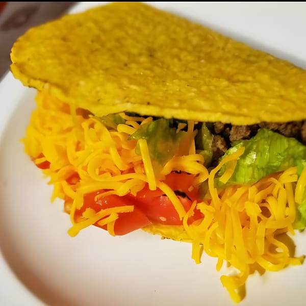 A hard-shell taco filled with ground beef, shredded lettuce, diced tomatoes, and cheddar cheese.