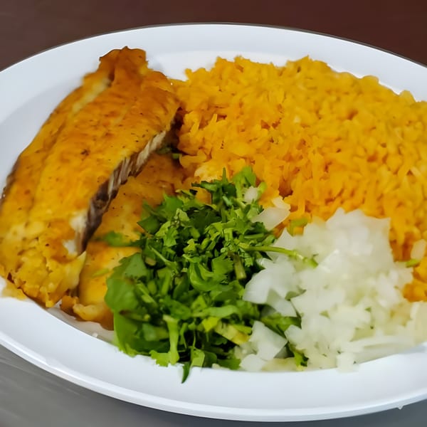 A white plate holds a golden-brown fish fillet, yellow rice, chopped cilantro, and diced white onions.