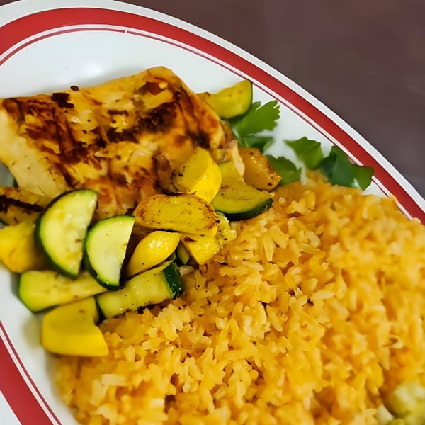 Grilled chicken with zucchini, yellow squash, and Mexican rice on a white plate with red trim.